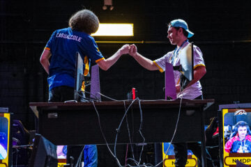 Two esports players fist bump over a desk with gaming monitors during a competition.