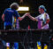 Two esports players fist bump over a desk with gaming monitors during a competition.