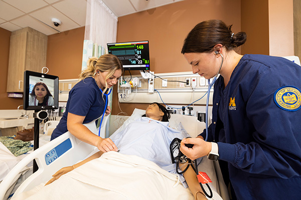 Two student nurses conducting simulated health care duties on a dummy.