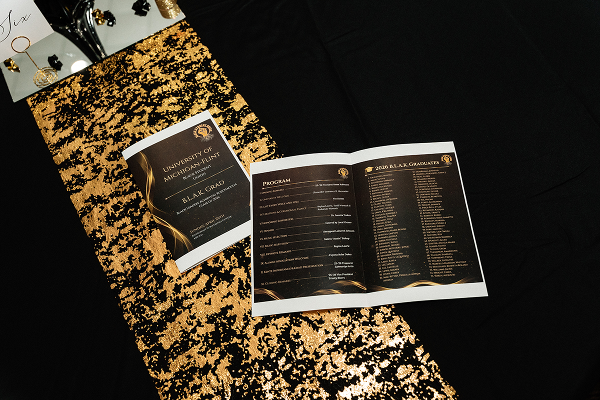 FLINT_BLAK Graduation Celebration 2026_0004 Program booklet for University of Michigan-Flint B.L.A.K. Grad event listing program details and 2026 graduates on a black and gold sequin table runner.