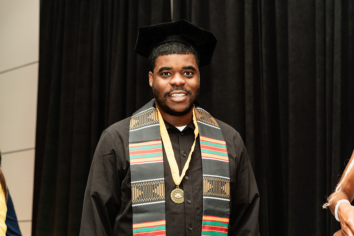 FLINT_BLAK Graduation Celebration 2026_0062 Person wearing a black graduation cap, black shirt, a colorful kente stole, and a gold medal on a yellow ribbon.