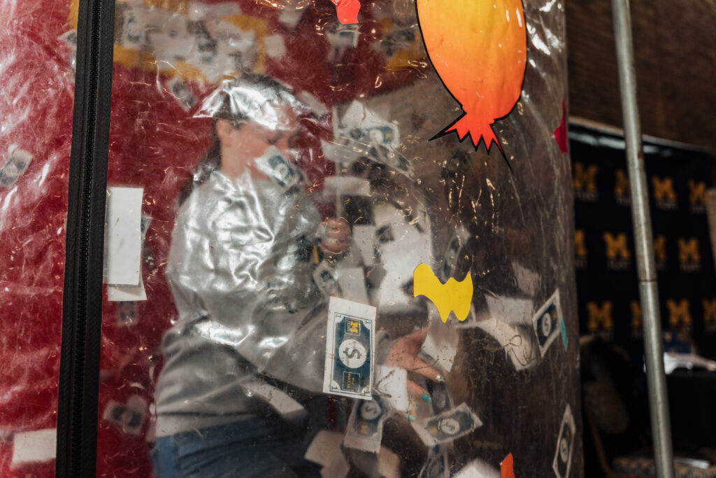 Person inside a transparent inflatable bubble filled with fake money and colorful paper cutouts.