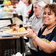 Person holding a plate of food at a cafeteria serving line.
