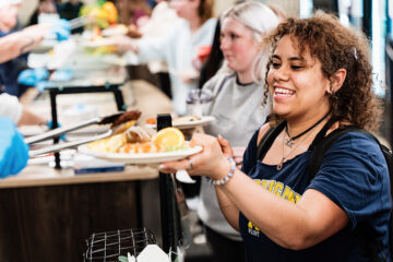Person holding a plate of food at a cafeteria serving line.