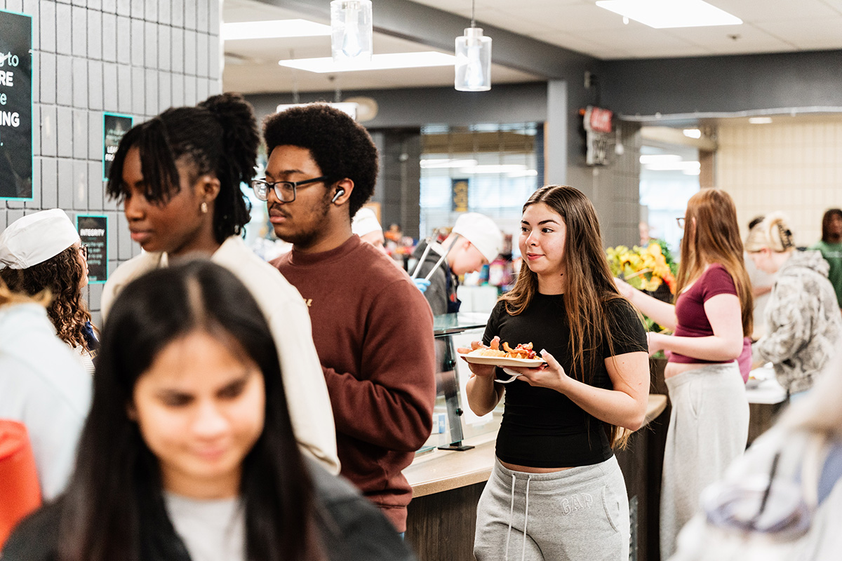 FLINT_Late Night Breakfast 2026_0007 People standing in line and holding plates in a cafeteria or dining hall.