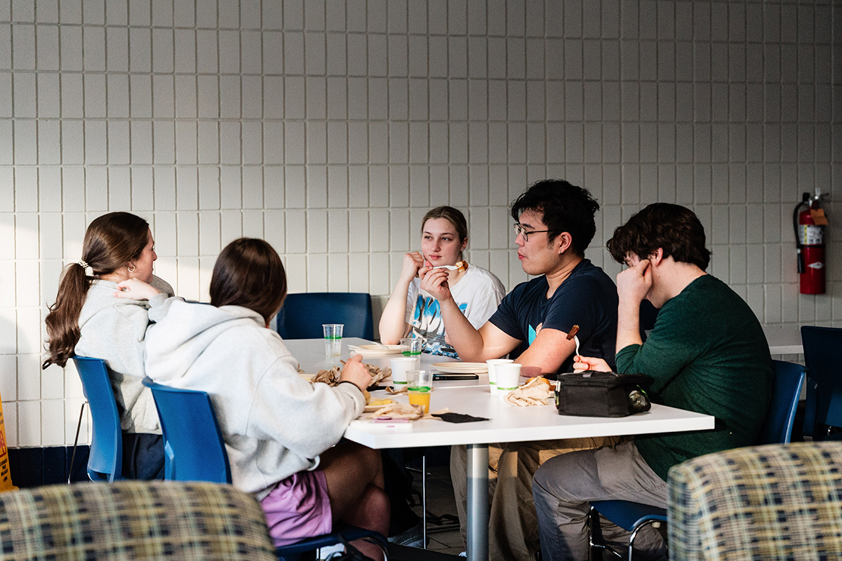 FLINT_Late Night Breakfast 2026_0022 Five people sitting around a table in a casual setting, eating and talking.