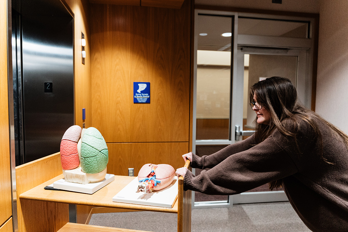 FLINT_Late Night in the Library 2026_0011 A person pushing a wooden cart with anatomical lung models in a hallway with wooden walls and an elevator.