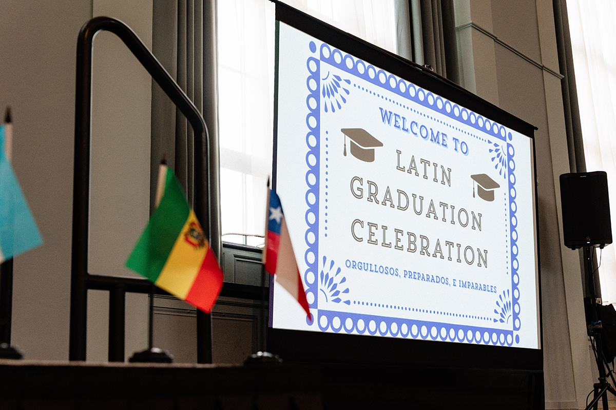 FLINT_Latin Graduation Celebration 2026_0004 Projection screen displaying "Welcome to Latin Graduation Celebration" with small flags in the foreground.