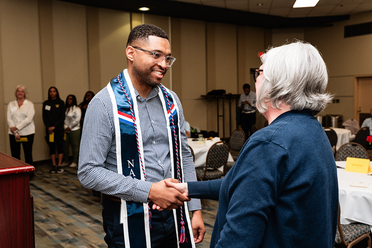 FLINT_Veterans Graduation Celebration 2026_0019 Two people shaking hands in a formal setting with tables and chairs in the background.