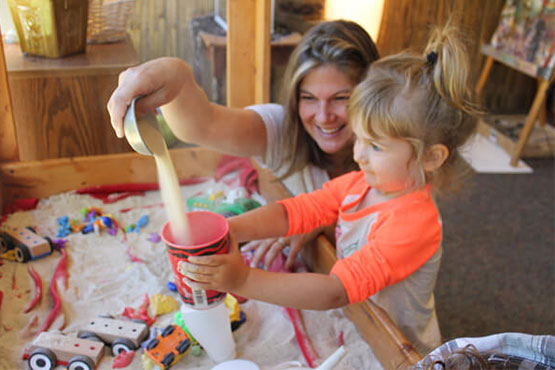 A teacher helping a young girl play with sand.