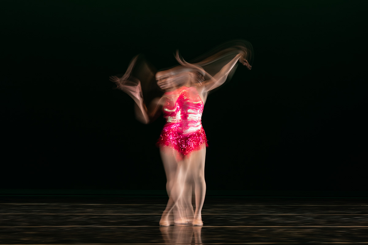 Blurred image of a dancer in a sparkling red outfit performing against a dark background.