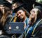 Group of graduates in caps and gowns, one holding a University of Michigan diploma cover.