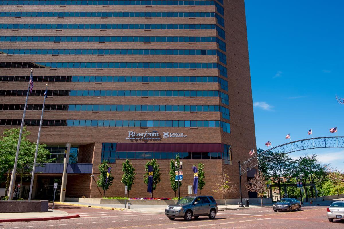 Exterior view of the University of Michigan-Flint School of Management. This view includes cars on Saginaw Street crossing beneath a black archway decorated with small American flags.