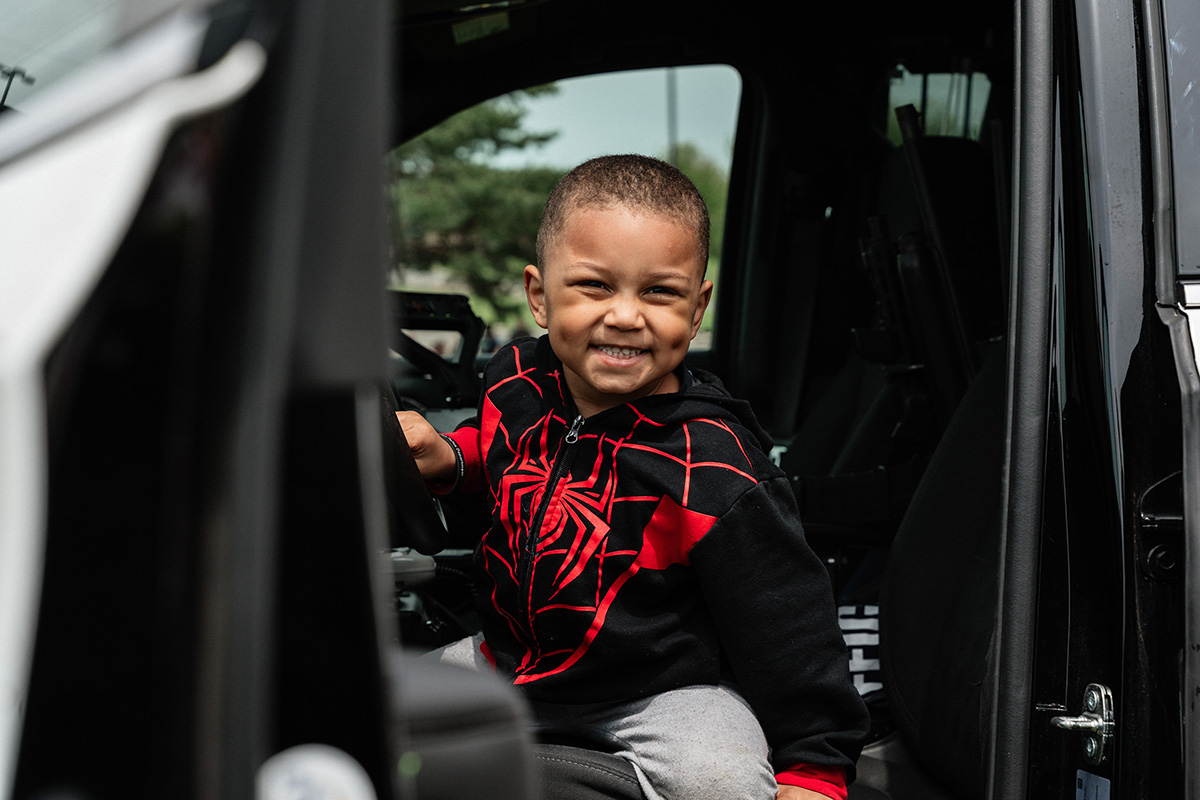 A child wearing a black and red Spider-Man hoodie sitting in the driver's seat of a vehicle.