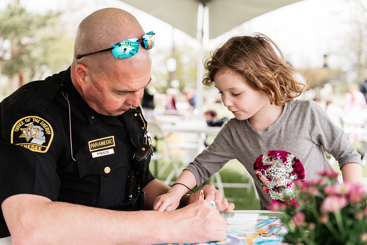 A paramedic in uniform playing a board game with a young child at an outdoor event.