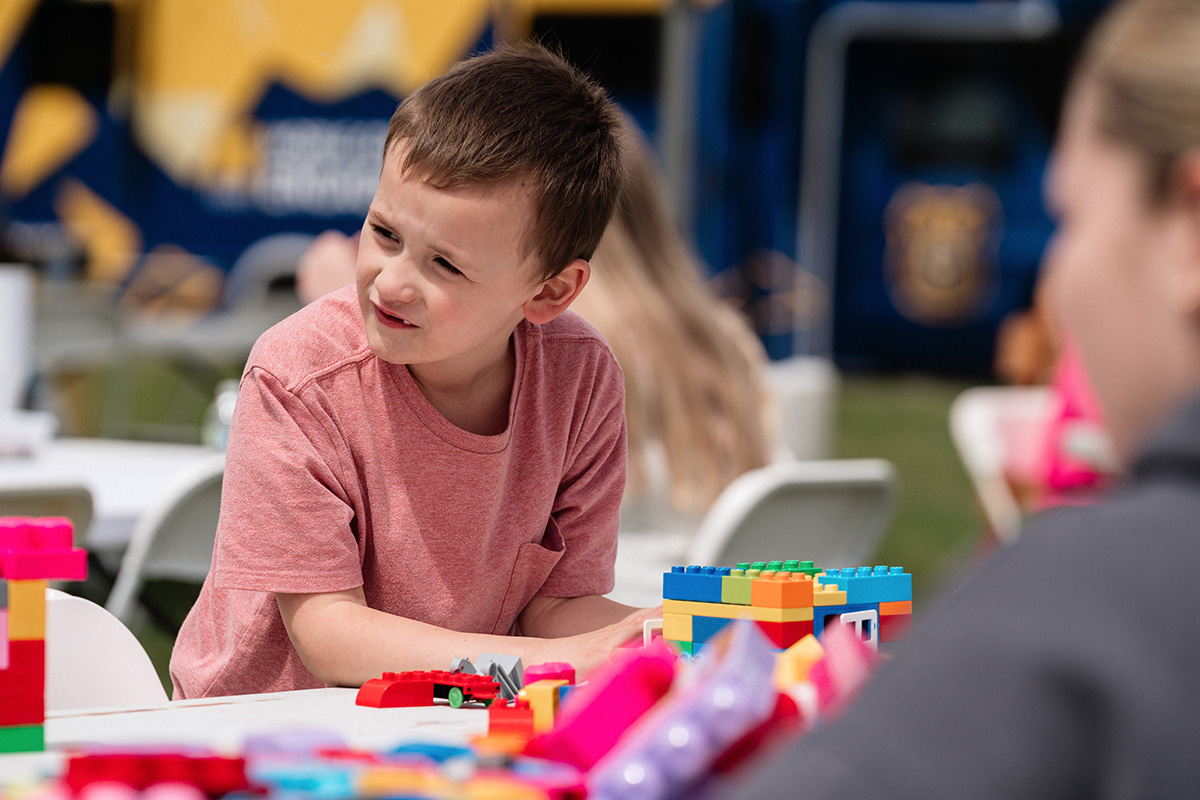 Child in a red shirt playing with colorful building blocks at a table outdoors.