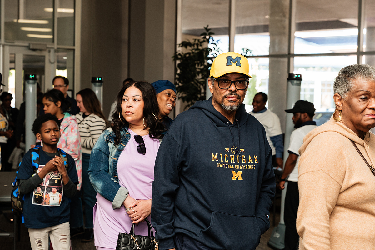 FLINT_Trey Day 2026_0003 People standing in line indoors, one person wearing a Michigan National Champions hoodie and yellow cap.