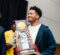 Three people holding an NCAA National Champion trophy with a basketball net attached.