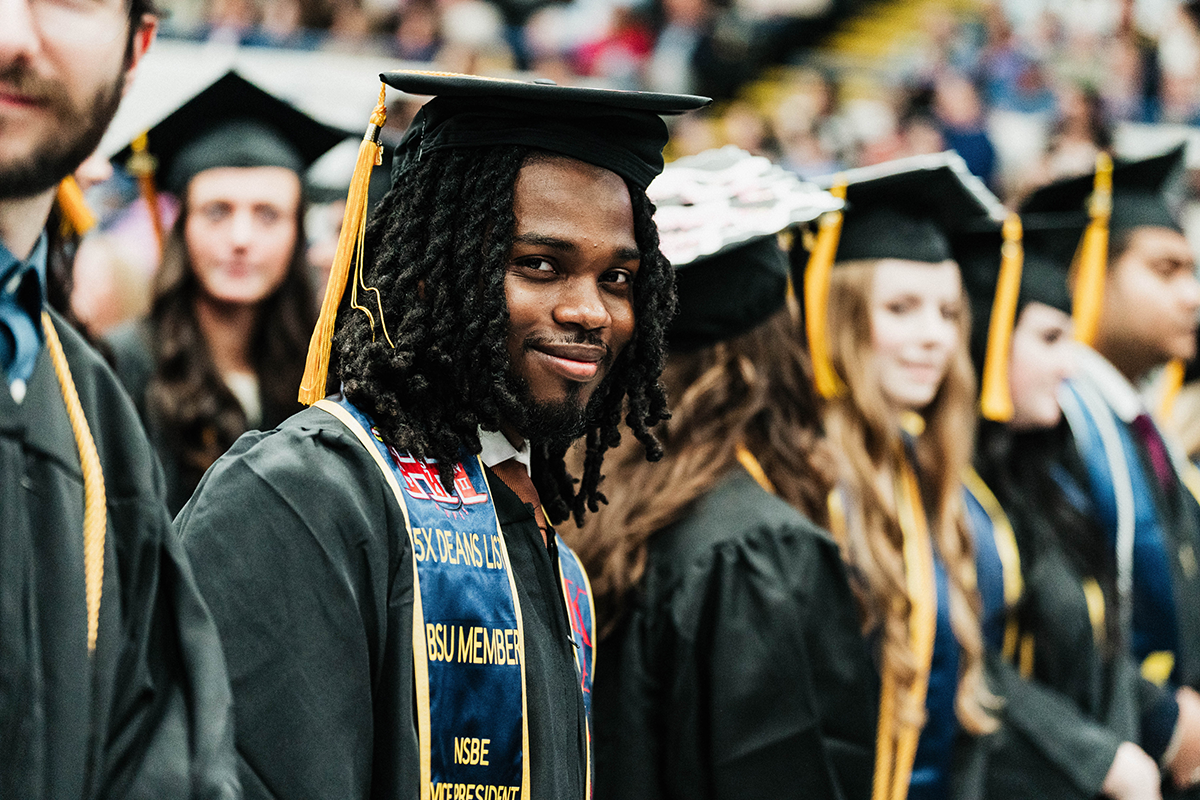FLINT_Winter Commencement April 2026_0005 Graduates in caps and gowns standing in a line at a graduation ceremony.