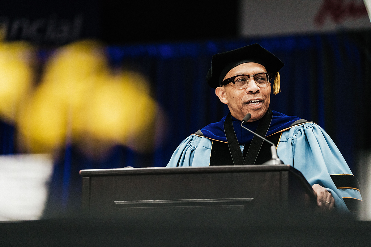 FLINT_Winter Commencement April 2026_0031 Person in academic regalia speaking at a podium during a graduation or academic ceremony.