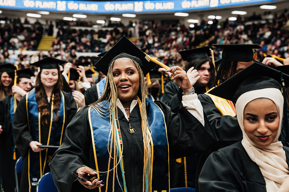 FLINT_Winter Commencement April 2026_0154 Graduates in caps and gowns at a university commencement ceremony, with one adjusting her tassel.