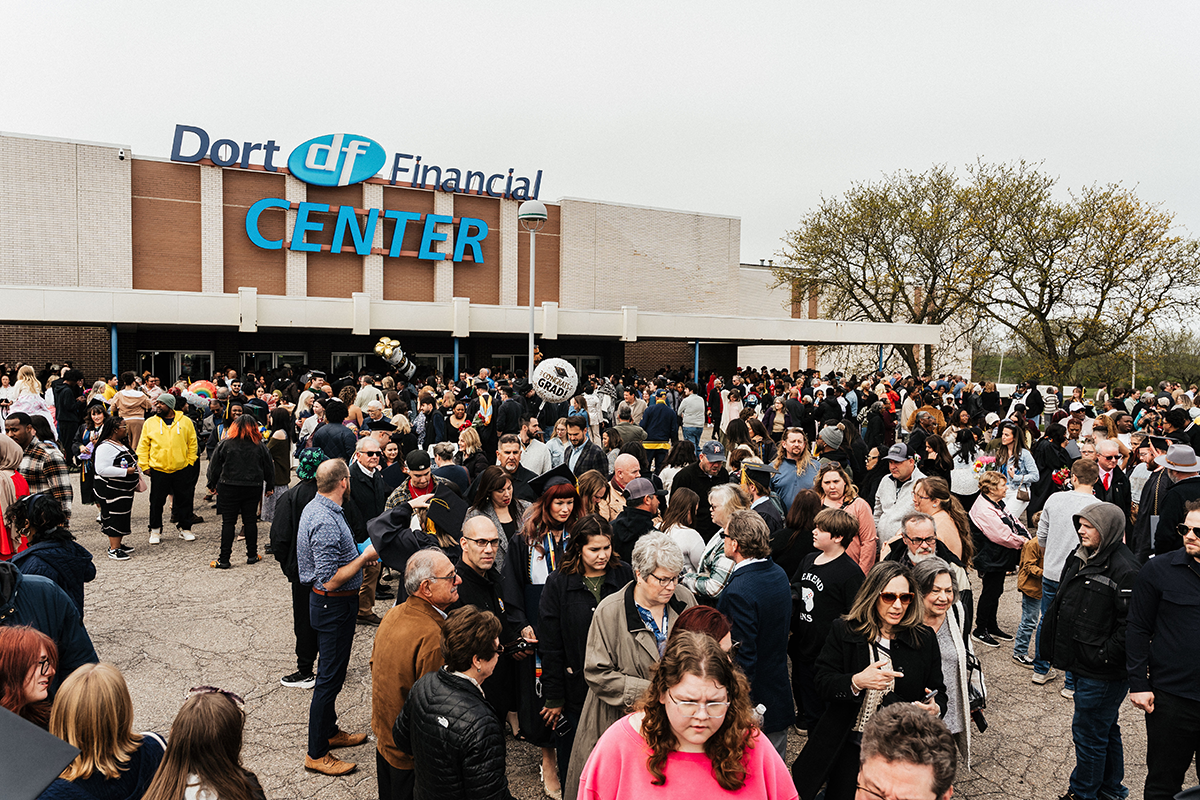 FLINT_Winter Commencement April 2026_0182 Large crowd of people gathered outside Dort Financial Center, some holding graduation balloons and flowers.
