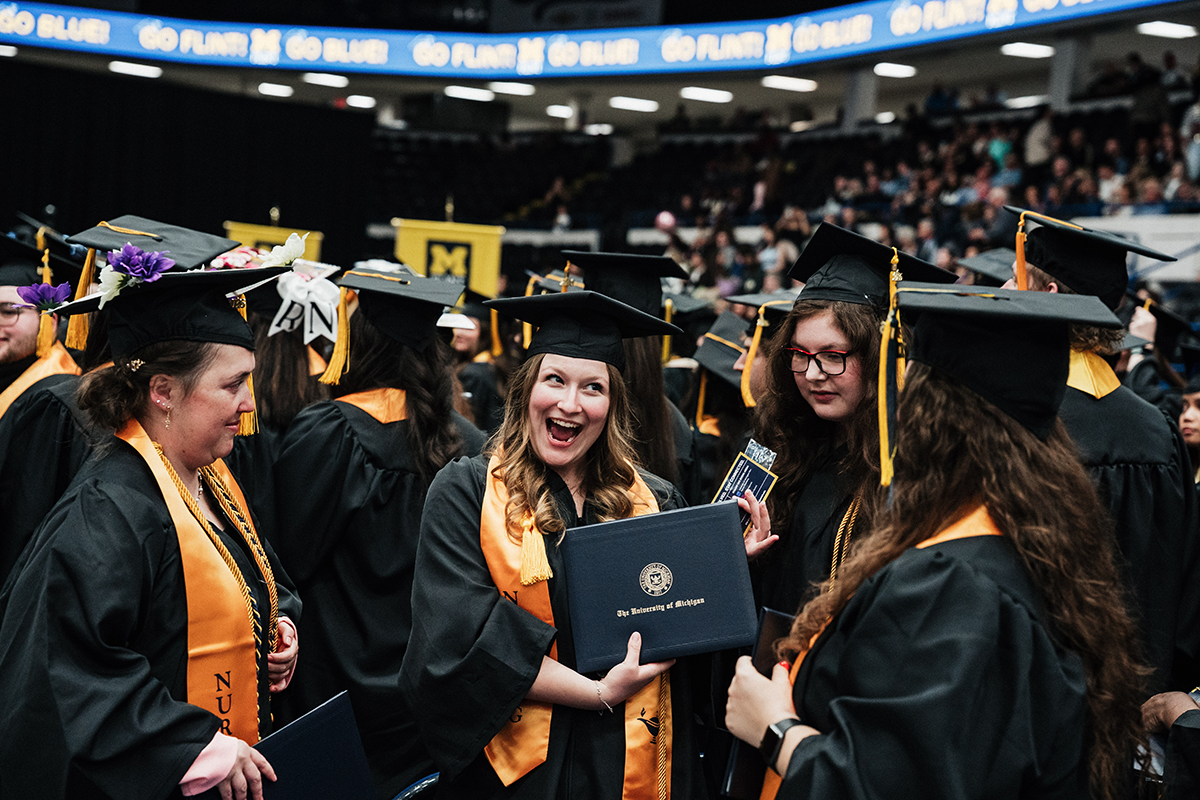 FLINT_Winter Commencement April 2026_0196 Graduates in caps and gowns holding diplomas at a University of Michigan graduation ceremony.