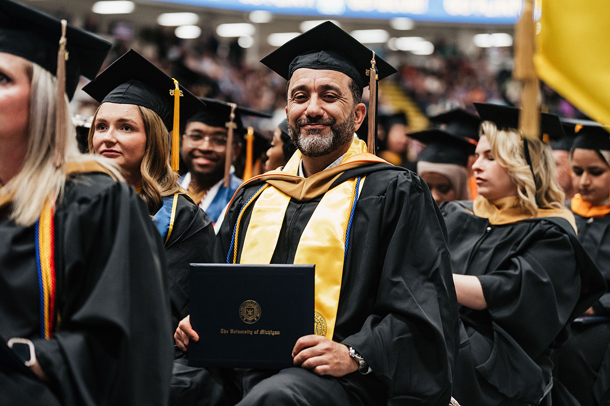 FLINT_Winter Commencement April 2026_0270 Group of graduates in caps and gowns, one holding a University of Michigan diploma.