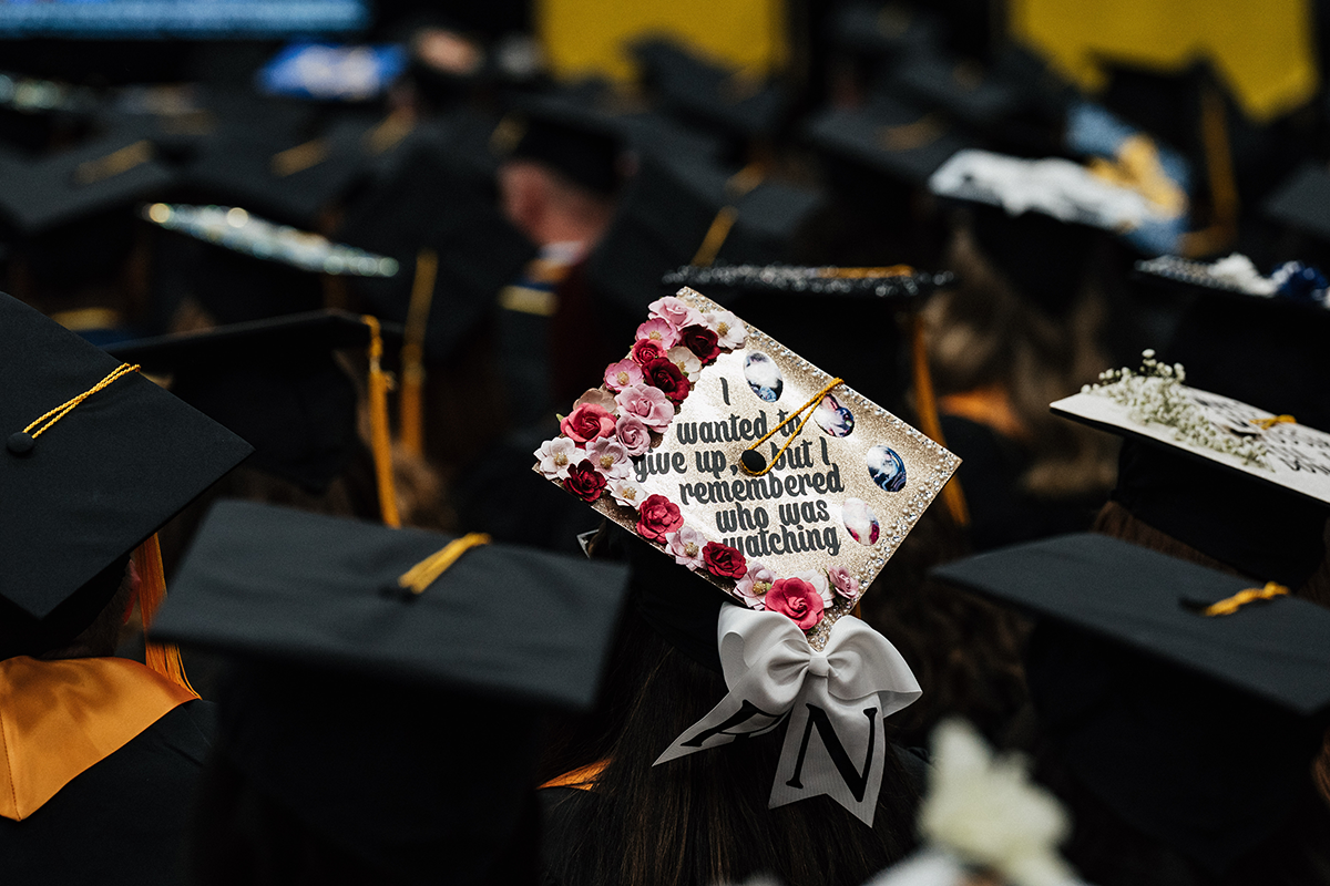 FLINT_Winter Commencement Caps April 2026_0002 Graduation cap decorated with flowers and the quote "I wanted to give up, but I remembered who was watching" among other graduates.