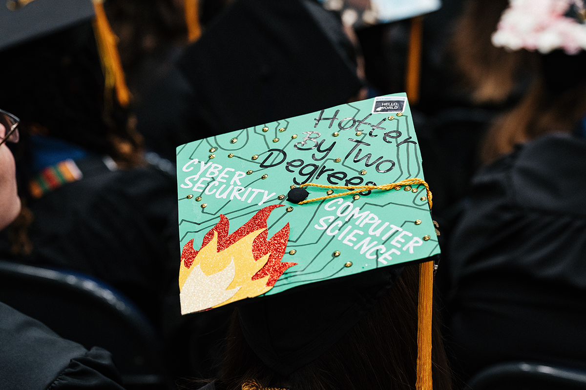FLINT_Winter Commencement Caps April 2026_0023 Graduation cap decorated with flames and circuit design, reading "Hotter By Two Degrees," "Cyber Security," and "Computer Science."