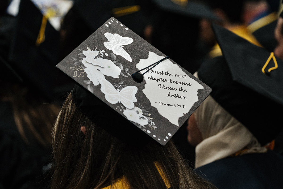 FLINT_Winter Commencement Caps April 2026_0028 Graduation cap decorated with white flowers and butterflies and the text "Trust the next chapter because I know the Author. - Jeremiah 29:11"