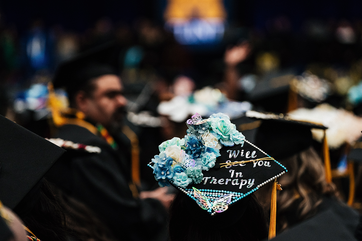 FLINT_Winter Commencement Caps April 2026_0032 Graduation cap decorated with blue flowers and butterflies, with the text "Will see you In Therapy" where "see" is crossed out.