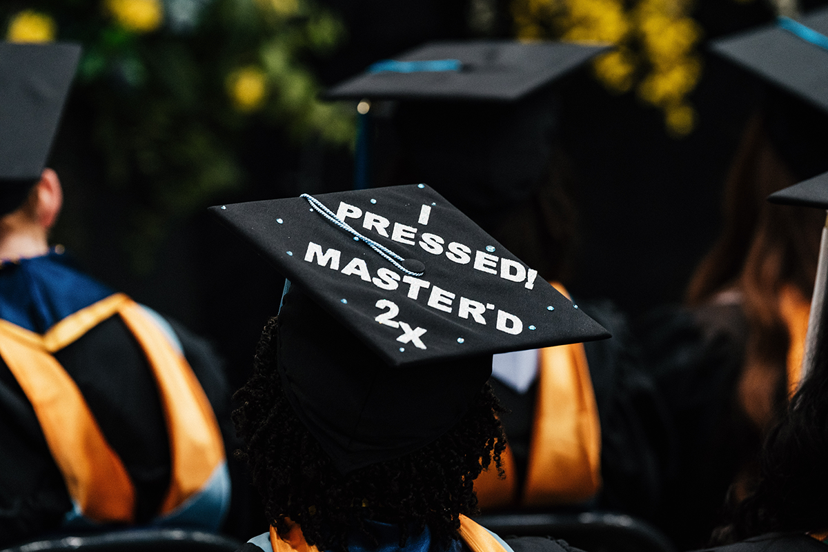 FLINT_Winter Commencement Caps April 2026_0043 Graduation cap decorated with the text "I PRESSED! MASTER'D 2x" worn by a graduate at a ceremony.