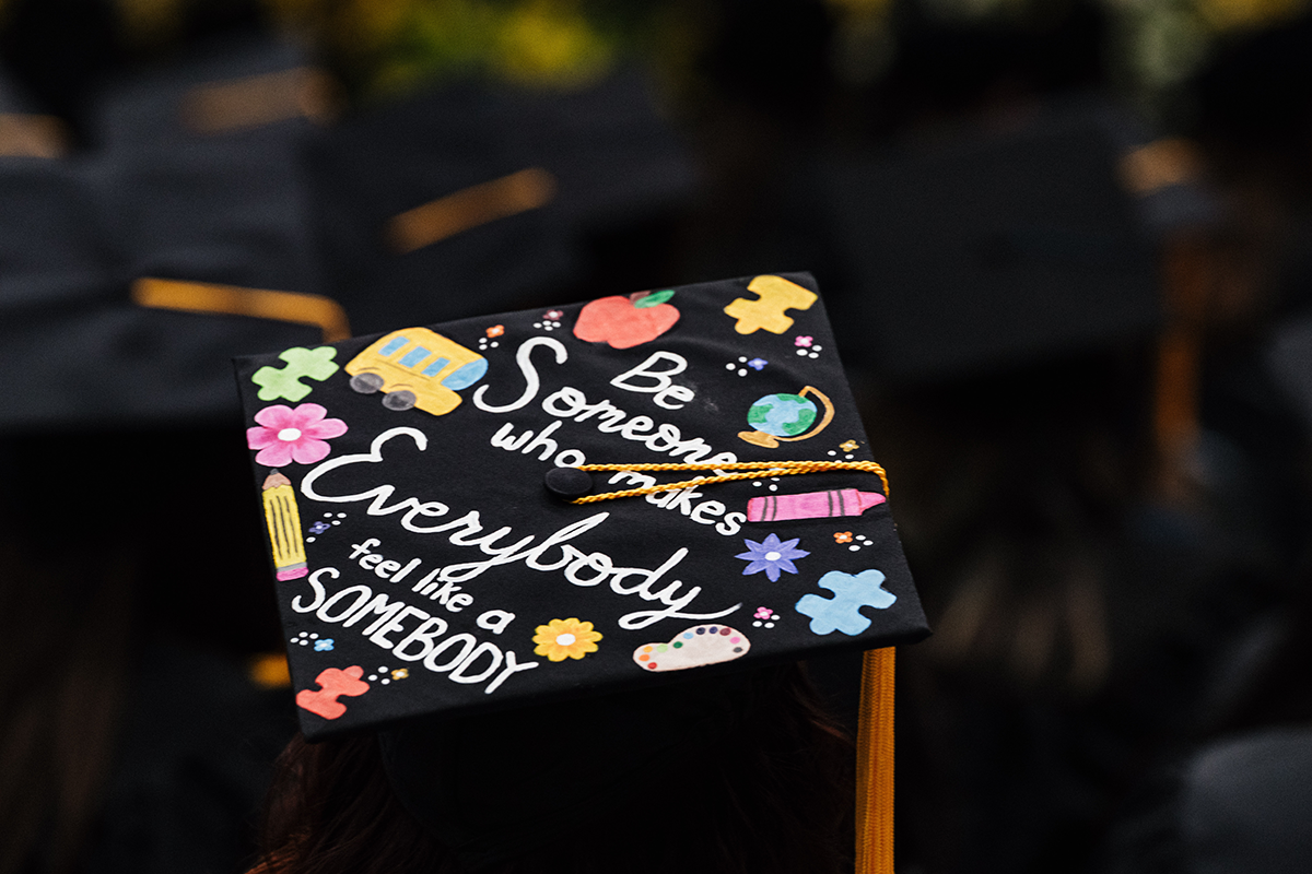 FLINT_Winter Commencement Caps April 2026_0056 Graduation cap decorated with colorful school-themed drawings and the text "Be someone who makes everybody feel like a somebody."