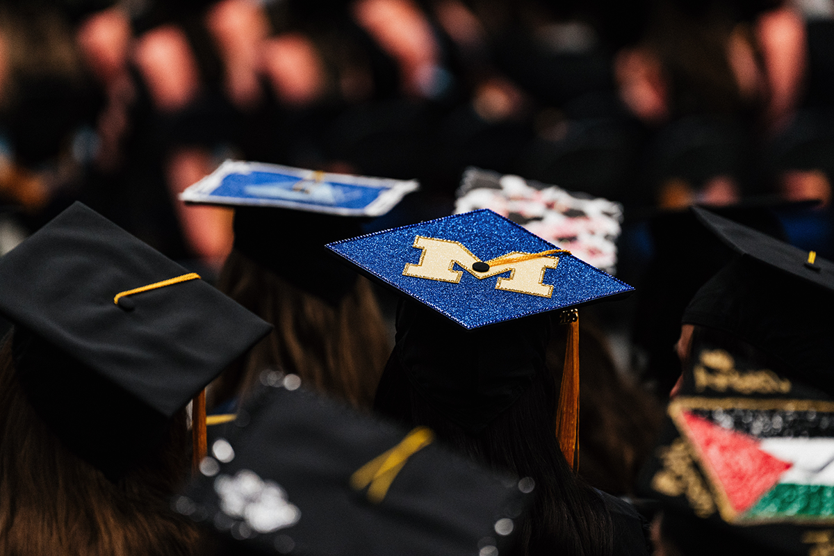 FLINT_Winter Commencement Caps April 2026_0061 Graduates wearing decorated caps, one with a large blue glittery "M" and others with various designs.