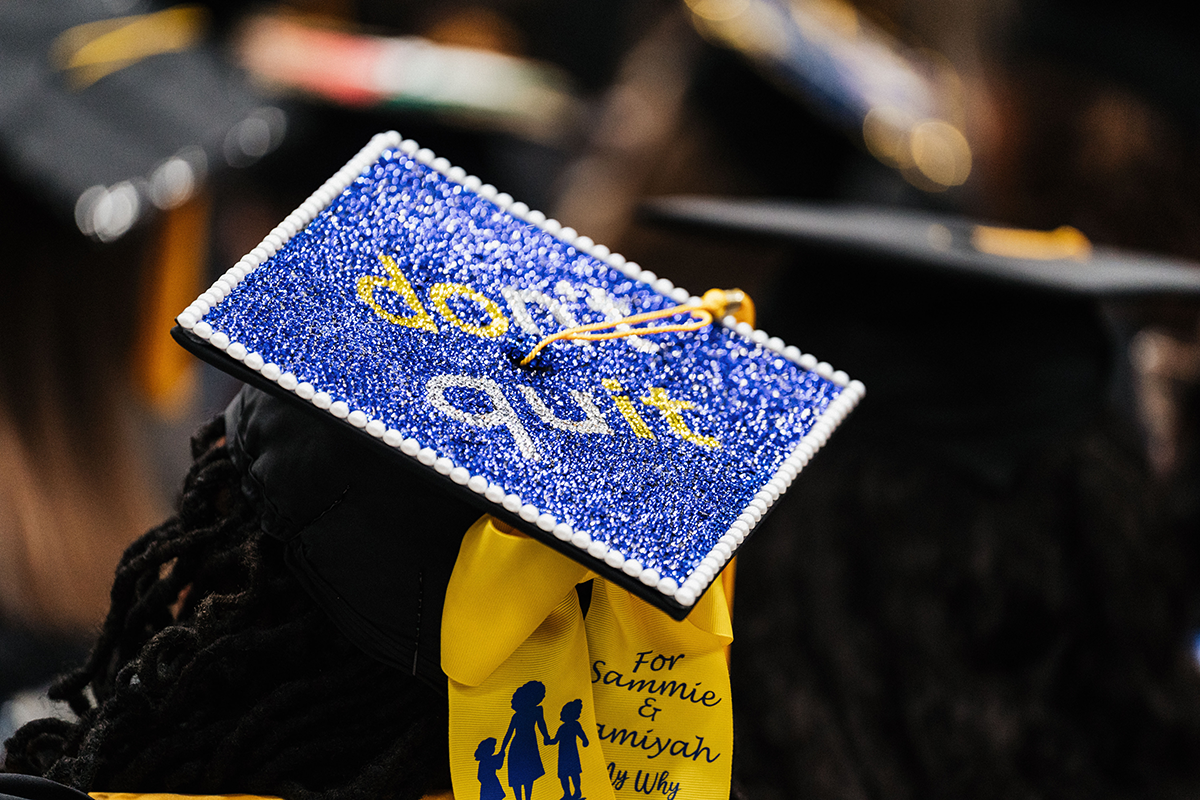 FLINT_Winter Commencement Caps April 2026_0063 Graduation cap decorated with blue glitter and white pearls, with the words "don't quit" and a yellow bow with a message for Sammie and Amiyah.
