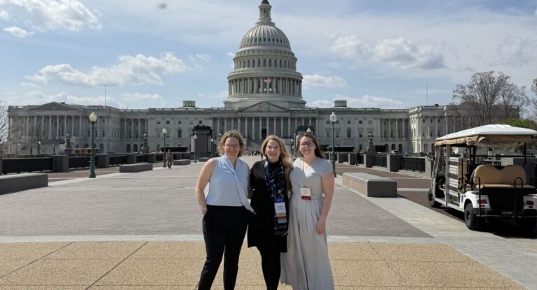 Three people standing in front of the United States Capitol building on a clear day.
