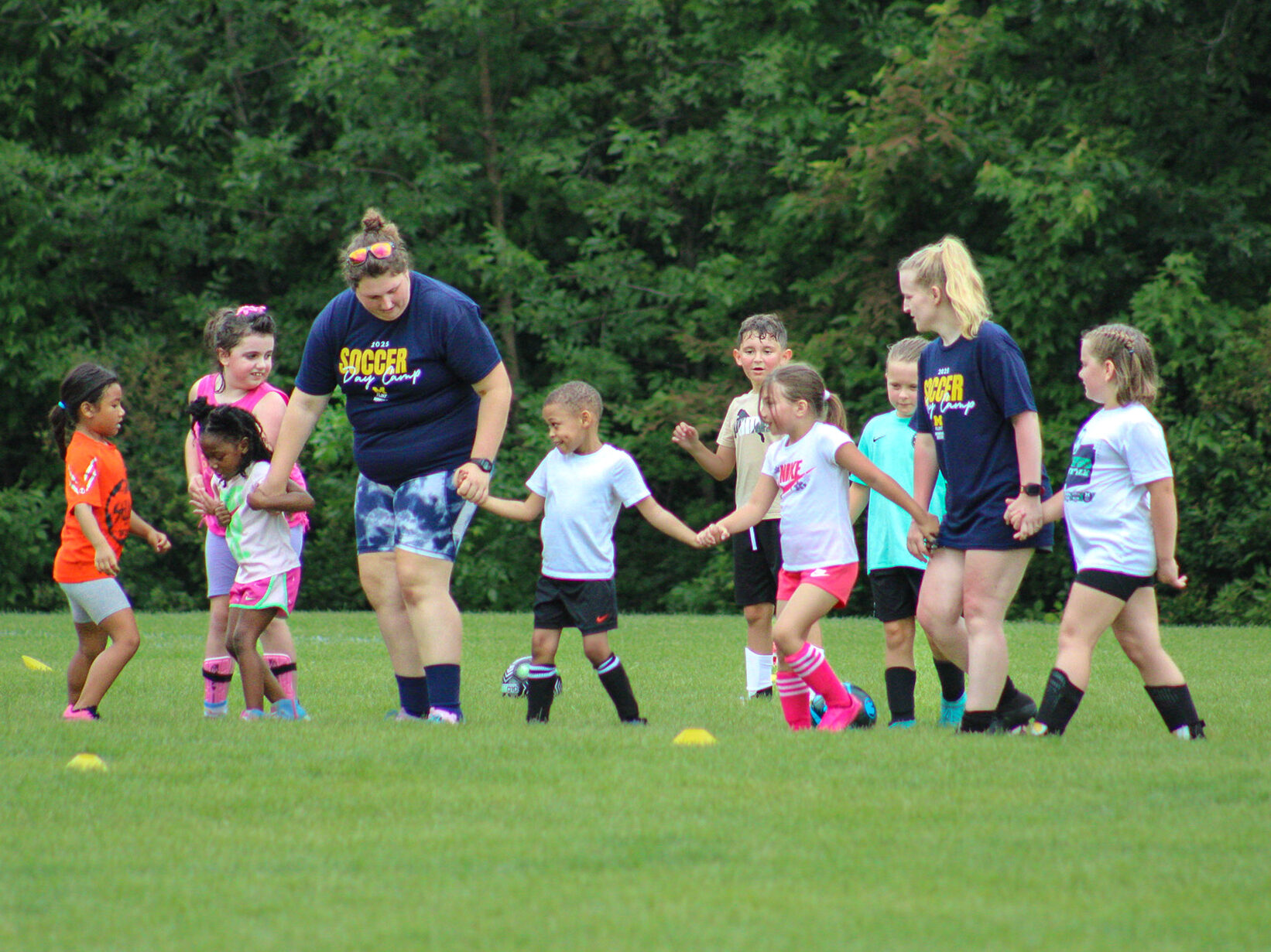 UM-Flint soccer players lead a group of camp goers in a drill on a soccer field.
