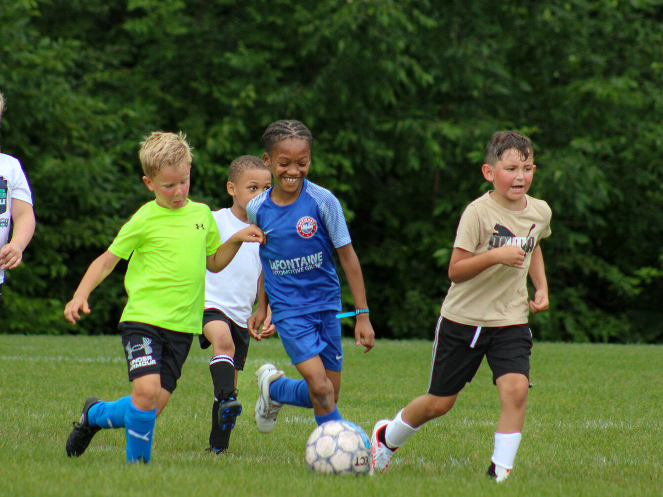 Young athletes kick a soccer ball while scrimmaging against each other.