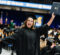Graduate in black cap and gown holding diploma and a card at a University of Michigan graduation ceremony.