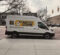 A white van with the text "THE HISTORY MACHINE" and a flower graphic, parked on a brick street near a building.
