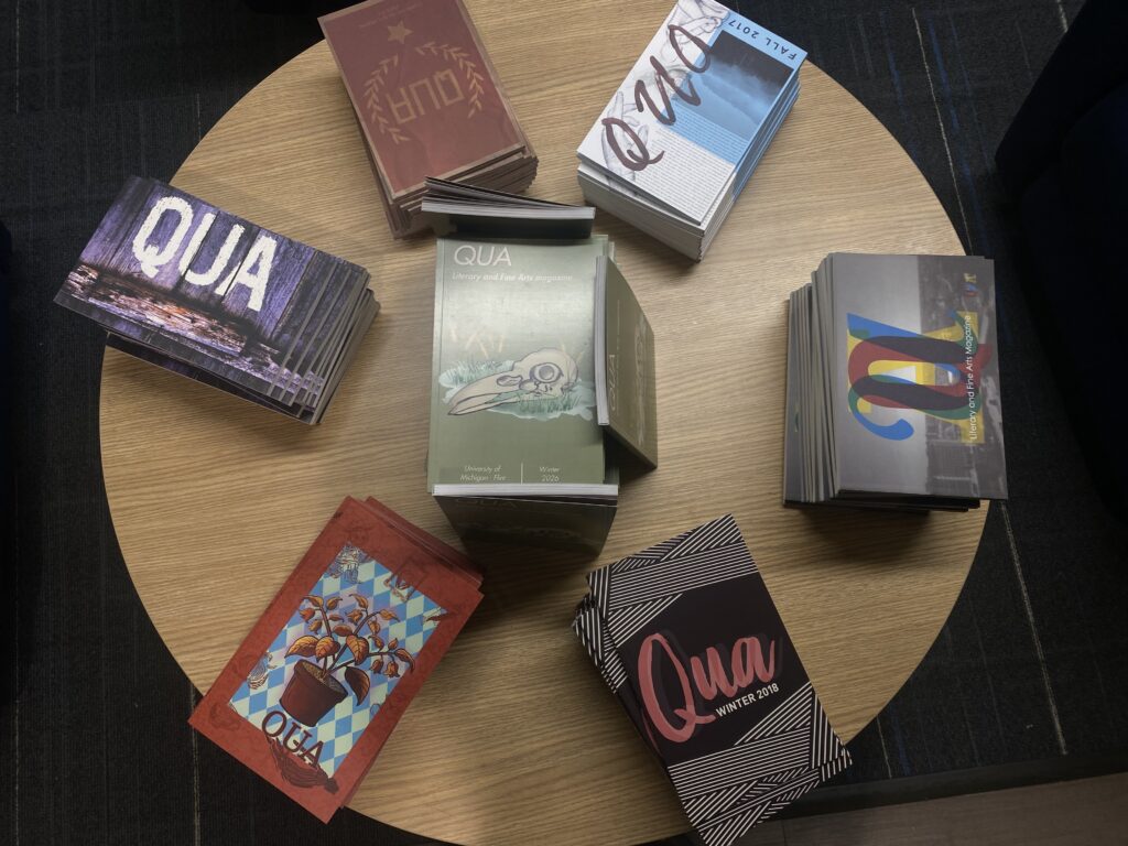 A round wooden table displaying a variety of magazines and booklets, primarily featuring the title "QUA" in different designs and colors.
