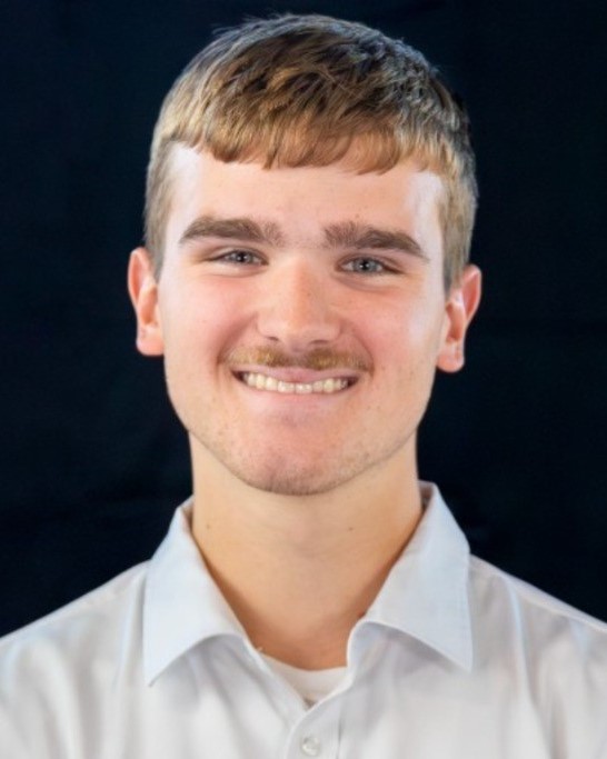 A young man smiles for a professional headshot. He has short brown hair and a thin mustache, and he is wearing a white, collared shirt.