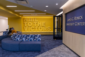 Interior of the James C. Renick University Center featuring a large yellow wall with the text "HAIL TO THE VICTORS" and a blue seating area with patterned cushions.