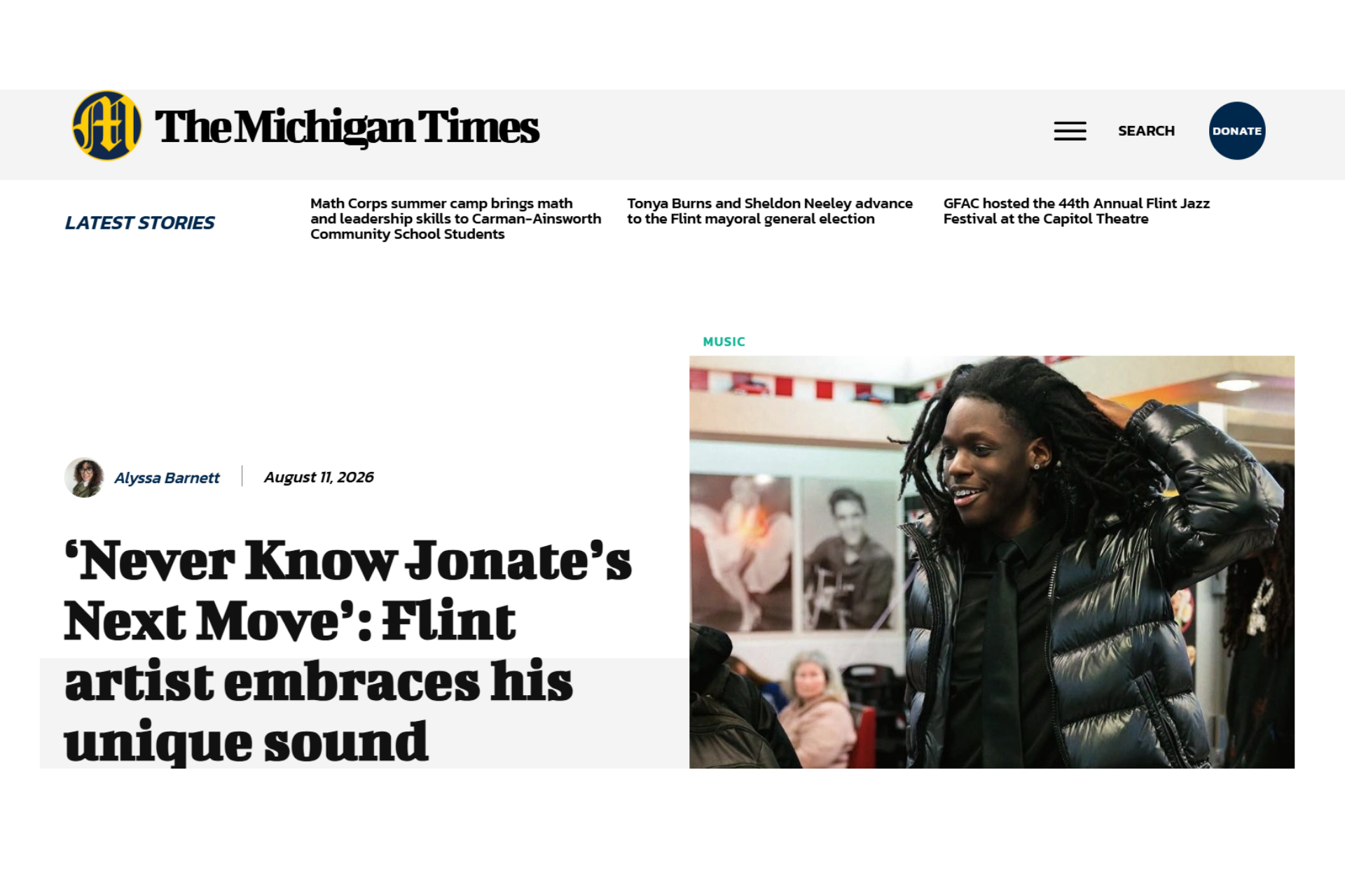Image of an article from The Michigan Times featuring a headline about Flint artist Jonate, with a photo of him smiling and wearing a black puffer jacket and tie.