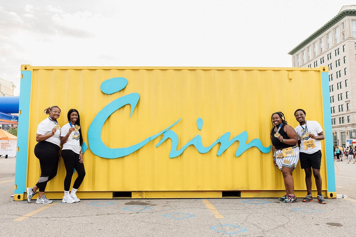 775319616_1508860957936501_6689143287407093919_n Four people stand in front of a large yellow shipping container with the word "Crim" written in blue. They are holding medals and smiling.