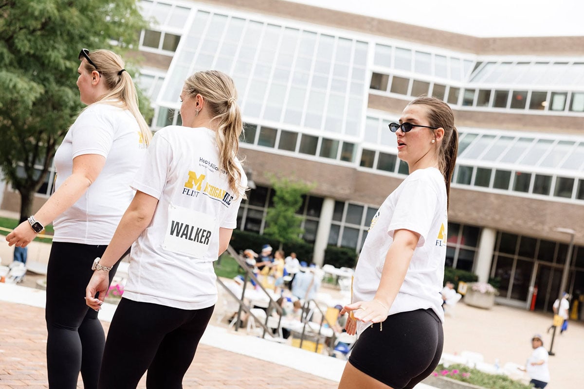 778139669_1508860917936505_2314644226375627385_n Three women in white t-shirts are participating in an event outdoors, with a building and trees in the background.