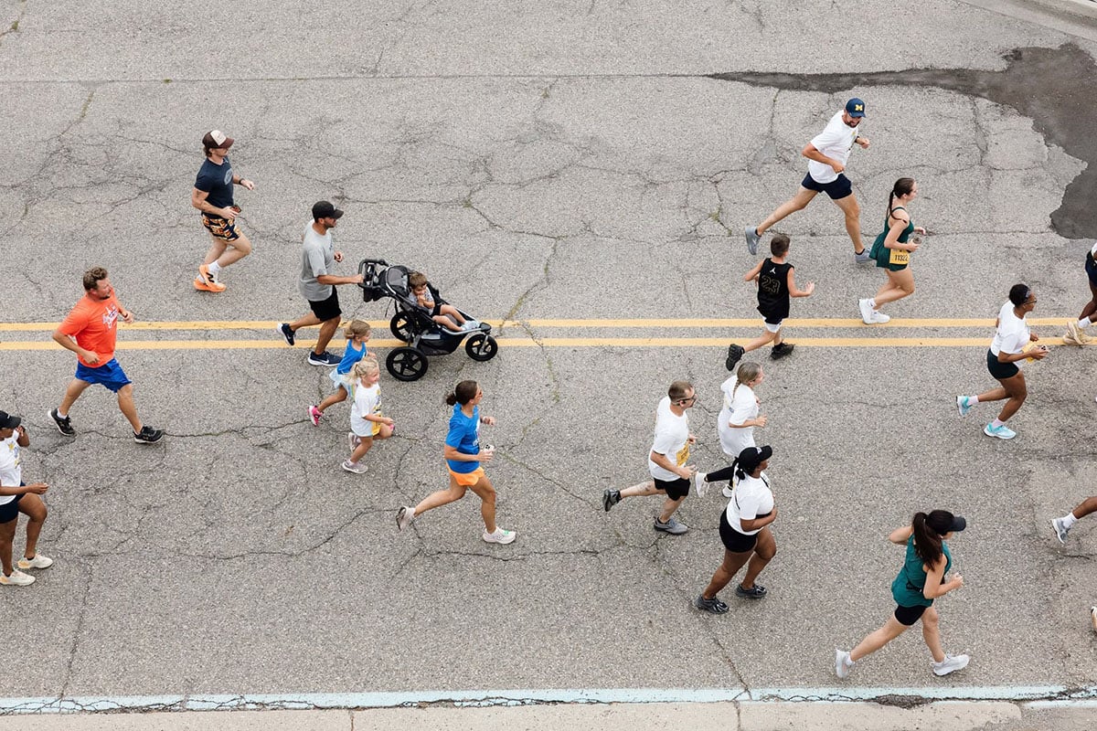 782511335_1508860581269872_8738987215669983143_n A group of people running on a cracked road, including adults and children, with one person pushing a stroller.