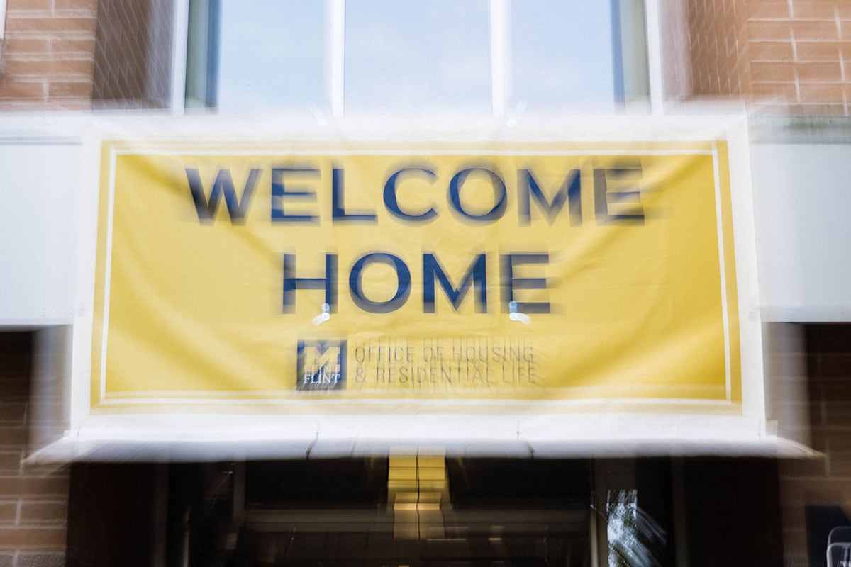 FLINT_2026 Move-In Day 0012 A banner that reads "WELCOME HOME" in large blue letters on a yellow background, with smaller text below stating "OFFICE OF HOUSING & RESIDENTIAL LIFE."
