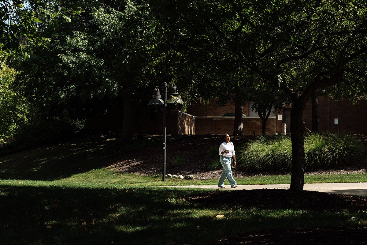 FLINT_First Day of Class Fall 2026_0045 A person walks along a path in a park-like setting, surrounded by trees and greenery.
